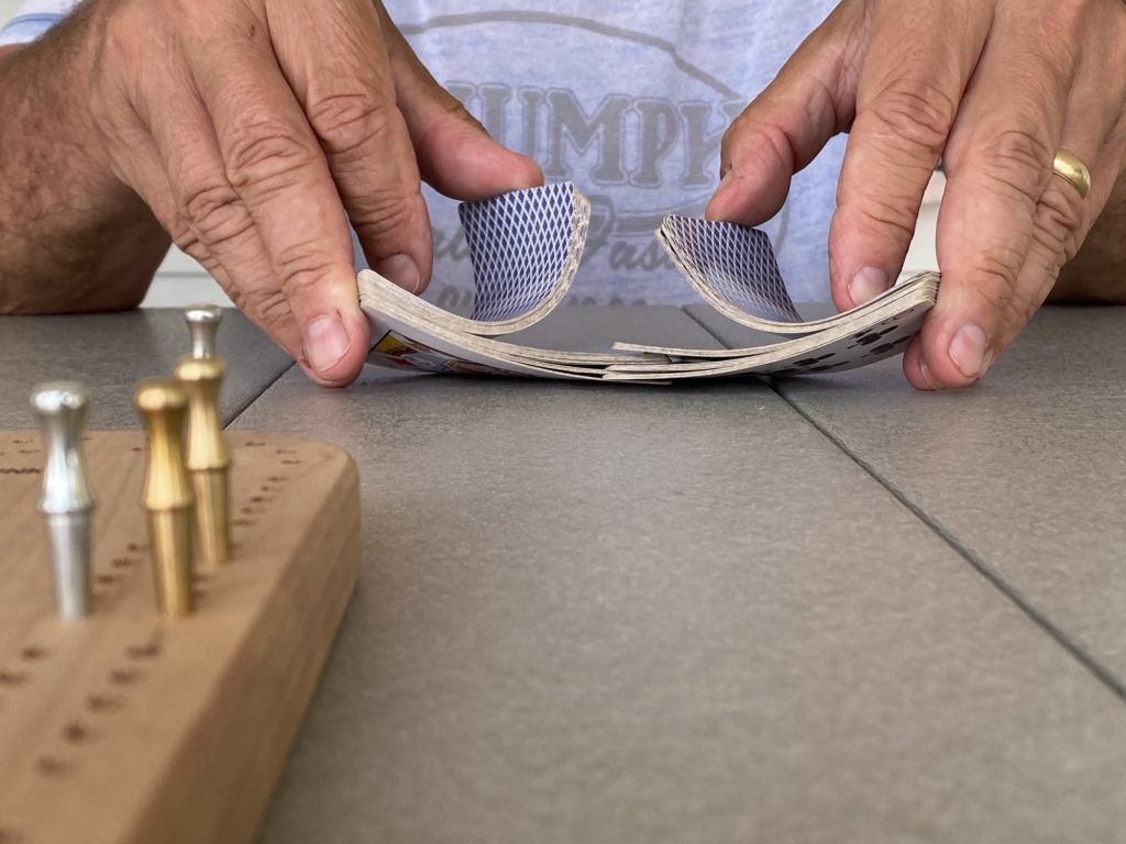 A man shuffles a deck of cards for a game of cribbage at the table