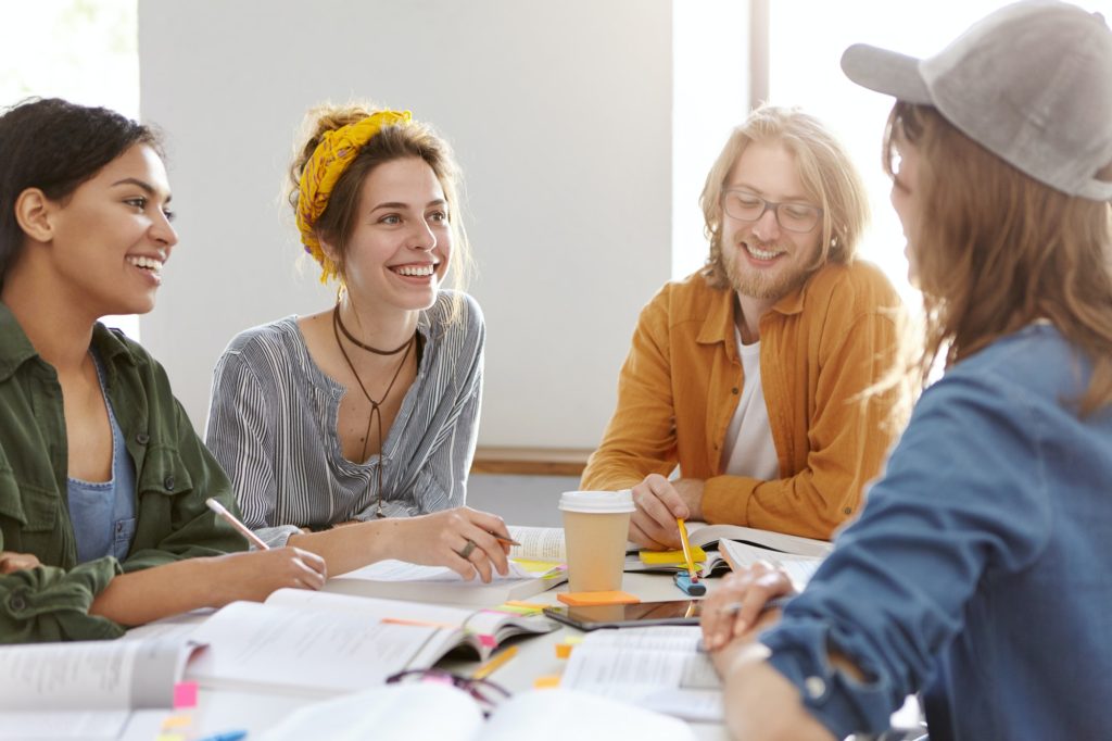 Horizontal portrait of multi-ethnic encouraged students surrounded with books having talk working to
